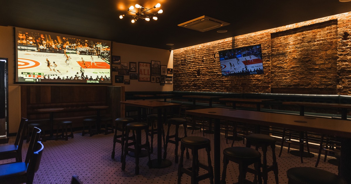 Cozy sports bar seating area with high tables and stools, and TVs displaying a basketball game
