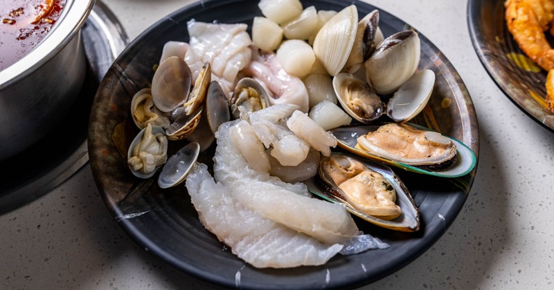 Plate of raw seafood featuring scallops, clams, mussels, and sliced fish