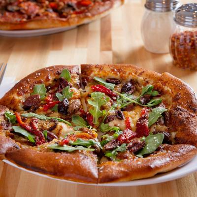 A pizza topped with arugula, roasted red peppers, olives, and melted cheese.