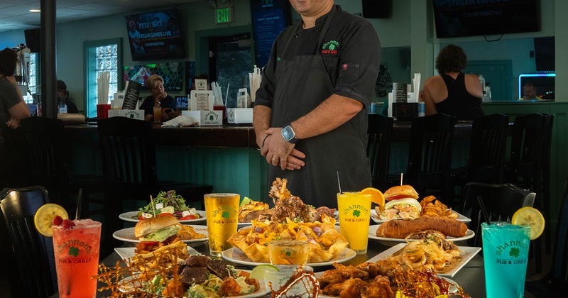 A chef stands behind a large table filled with assorted pub dishes and colorful drinks