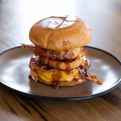 A plate holds BBQ Bacon Burger on a wooden table.