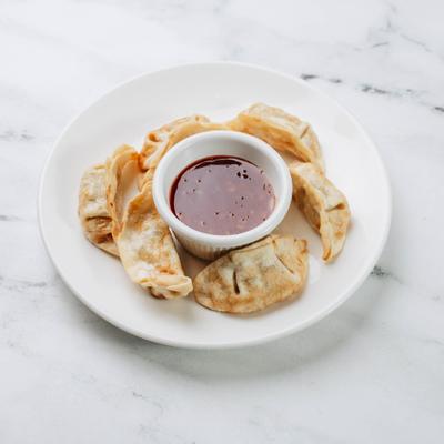 Pot stickers arranged around dipping sauce on white plate.