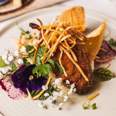 Breaded chicken topped with crispy fries, garnished with flowers and greens.