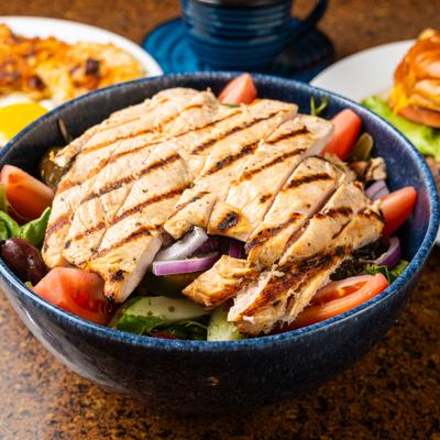Bowl of salad topped with sliced grilled chicken.