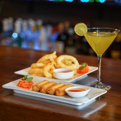 Spring rolls served with sweet chili sauce, a plate of calamari rings, and a cocktail.