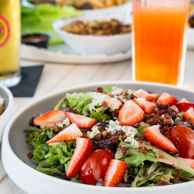Fresh salad with strawberries, tomatoes, and greens sits beside colorful iced drinks.