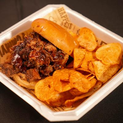 Pulled pork sandwich served with chips.