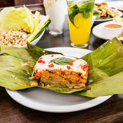 Thai curry dish wrapped in a banana leaf, served with drinks and sides.