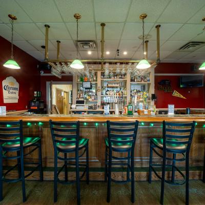 A wooden bar counter with four dark metal bar stools and pendant lights.