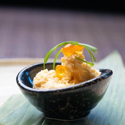 A black speckled bowl holds a creamy dish topped with orange fish roe and green herbs.