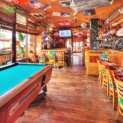 Warm, rustic bar with vibrant decor, pool table, colorful chairs, and wall art