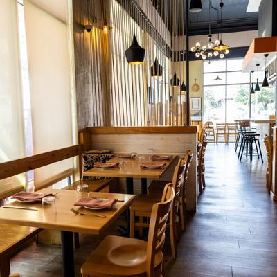 Restaurant interior with wooden tables, pendant lights, and large windows.