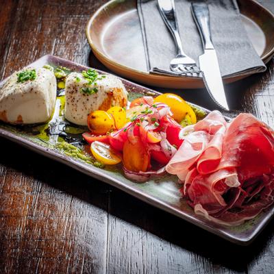 Burrata and prosciutto board paired with colorful tomatoes.