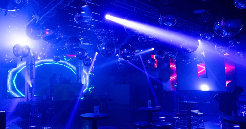 A nightclub with a DJ booth and reflective disco balls under vibrant blue and purple lighting