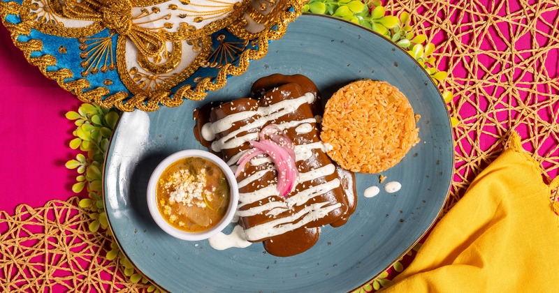 Enchiladas served with mole sauce, rice, and soup