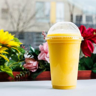 Mixed fruit smoothie in a clear plastic cup, with floral arrangements in the background.