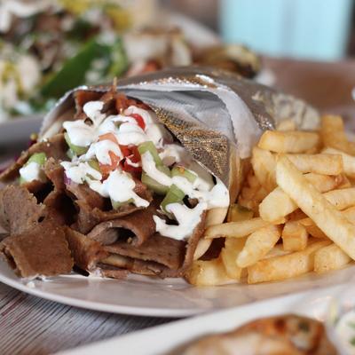 A gyro wrapped in foil, sits on a plate next to  golden fries.