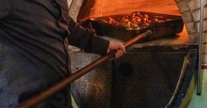 A chef placing meat in the wooden oven