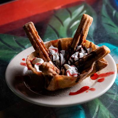 Churros served inside a fried tortilla bowl with whipped cream and drizzle of sauces.