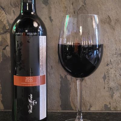 A bottle of syrah wine from 2022, beside a filled glass.