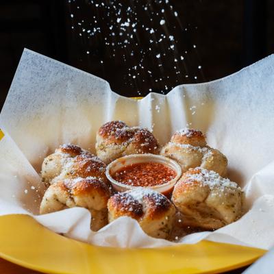 Garlic knots with dip being sprinkled with parmesan.