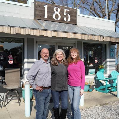 The owners posing with their adult child in front of the restaurant.