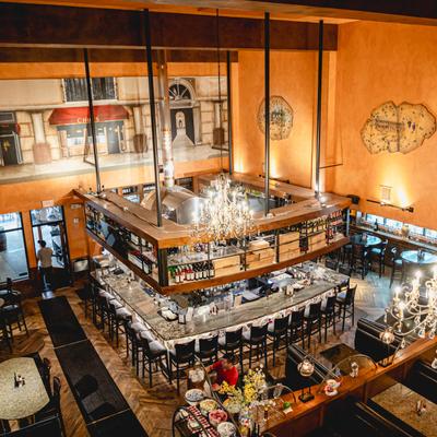 Restaurant interior with a bar, chandeliers, and a mural.