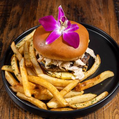 Burger with slaw and fries topped with a purple orchid on a black plate.