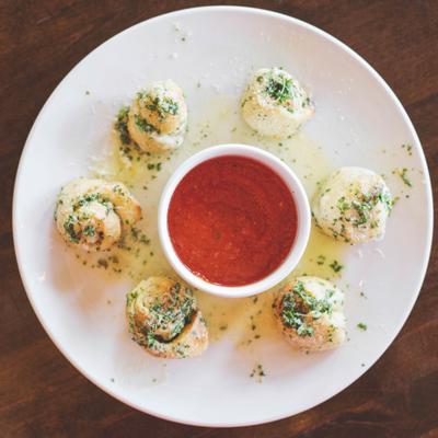 Eight garlic bread balls arranged around a small bowl of red marinara sauce.