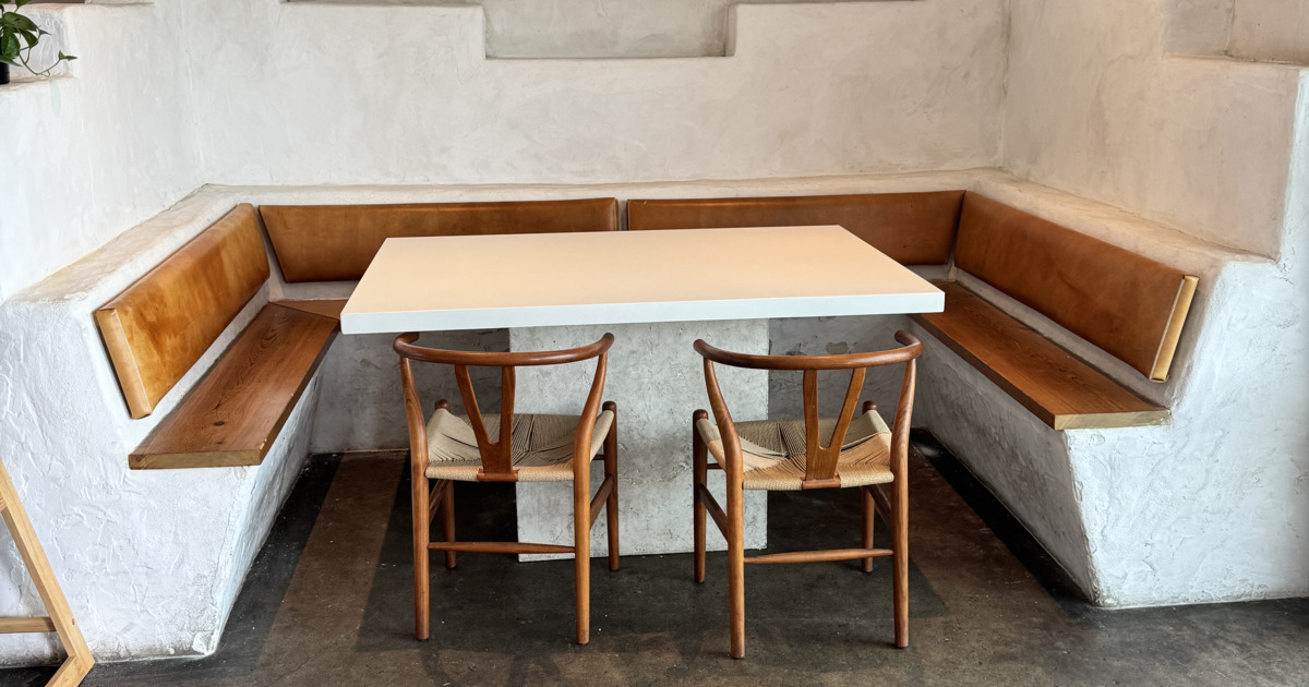 Corner booth with a modern white table, flanked by wooden benches and two chairs