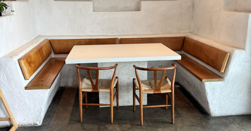 Corner booth with a modern white table, flanked by wooden benches and two chairs