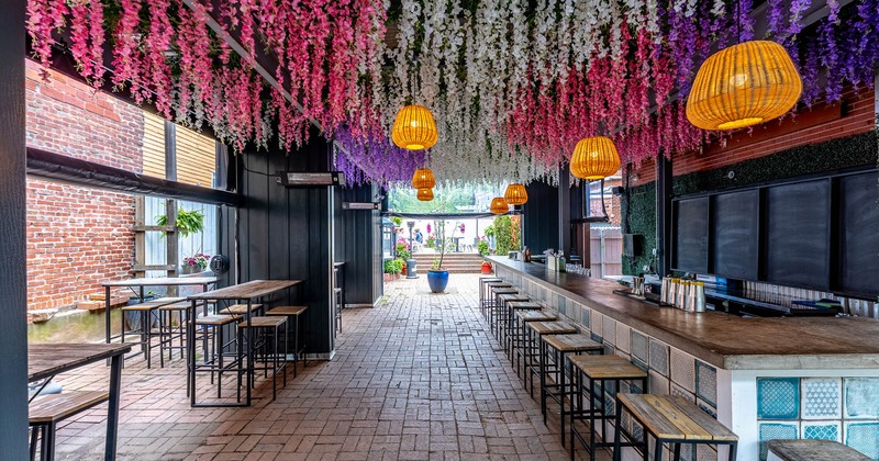 Outdoor patio bar with a colorful floral ceiling, rattan lighting, and modern seating