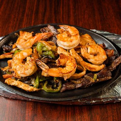 Platter of Fajitas featuring grilled shrimp, steak, chicken, and sautéed peppers.