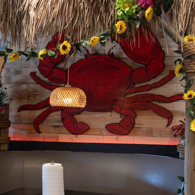Restaurant booth  with a red crab mural on wood wall, thatched roof and faux flowers.