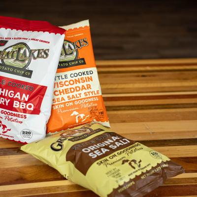 Two bags of chips standing upright on a wooden table, with a third bag lying beside them.
