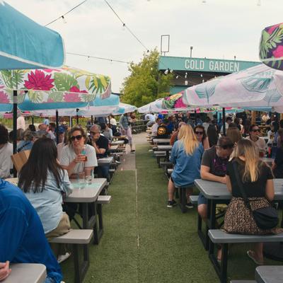 Crowded beer garden with picnic tables and floral umbrellas.