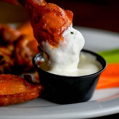 A wing being dipped in a sauce, close up.