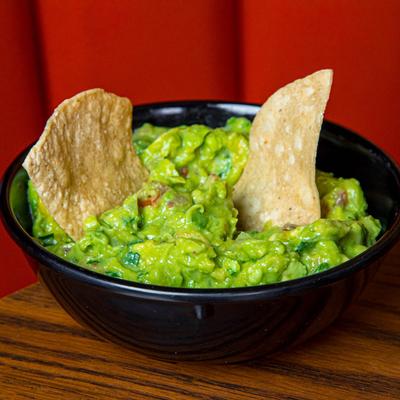 A bowl of guacamole topped with two tortilla chips.
