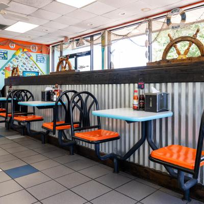 Nautical-themed seafood restaurant interior with orange chairs, corrugated metal, and ship wheels.