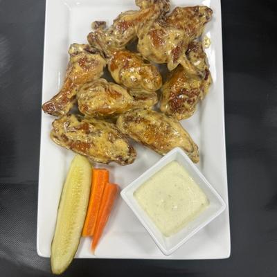 Chicken wings smothered in sauce, with carrots, pickle, and dip.