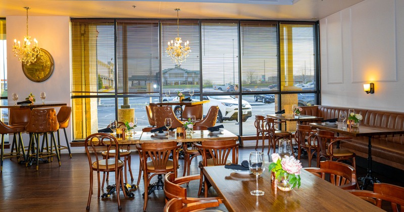 Elegant restaurant interior with wooden tables, cushioned seating, chandeliers, and large windows