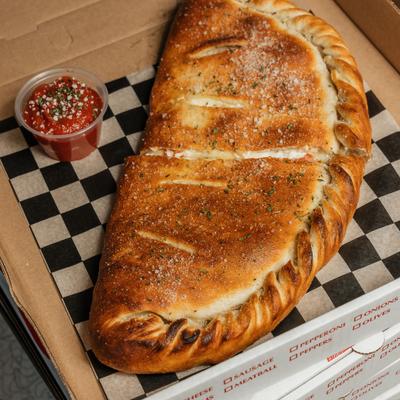 A calzone served on a black checkered paper with a side of marinara sauce.