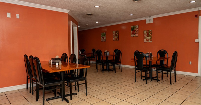Restaurant interior with orange walls, tiled floor, and multiple tables with black chairs