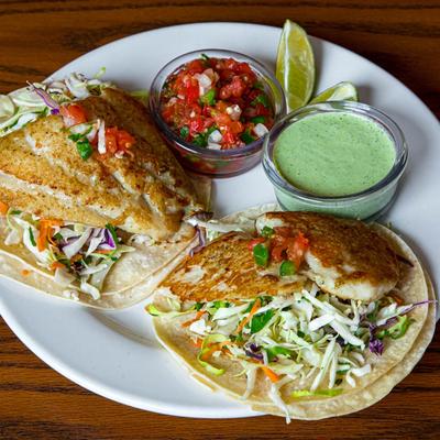 Fish tacos with coleslaw, served with salsa and green sauce.