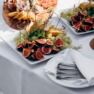 Catering platter of appetizers, figs, grapes, and a charcuterie board in an event setting.