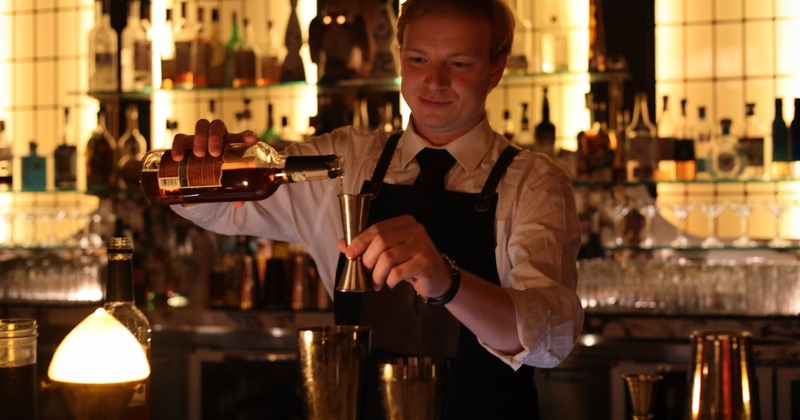Bartender pouring liquor from a bottle into a jigger behind a bar
