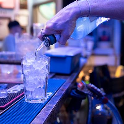 Bartender pouring a drink into a glass filled with ice.