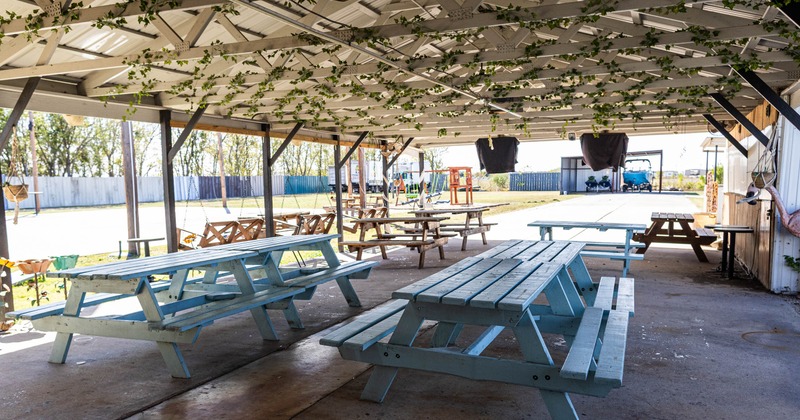 Exterior, covered seating area, large wooden tables with benches, concrete flooring