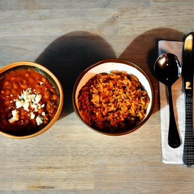 Spanish rice and pinto beans served on a wooden table next to utensils.