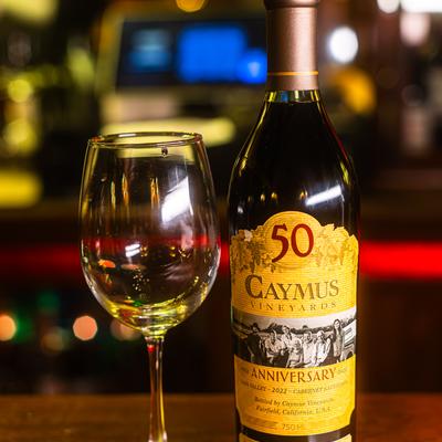 A wine bottle and glass stand on a dark counter.